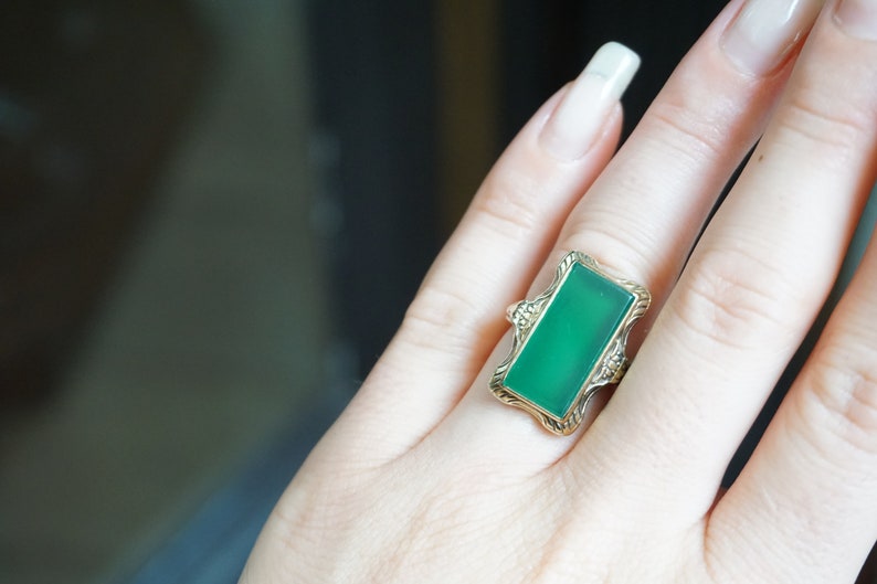 May include: A gold ring with a rectangular green gemstone set in a decorative frame.