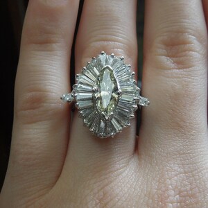 Op de afbeelding: Een ring met een marquise-geslepen diamant met een halo van kleinere diamanten. De ring is gezet in een band van wit metaal.