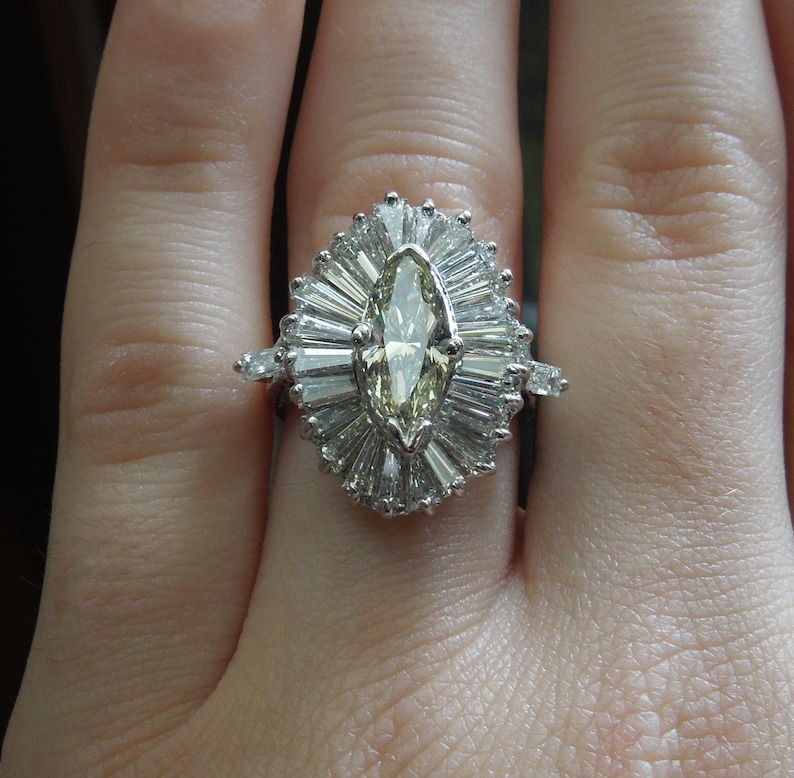 Op de afbeelding: Een ring met een marquise-geslepen diamant met een halo van kleinere diamanten. De ring is gezet in een band van wit metaal.