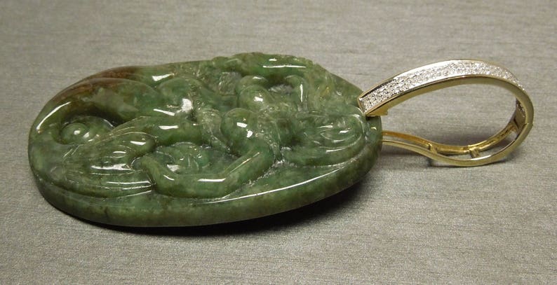 May include: A green jade pendant carved with a dragon design, set in a gold frame with a diamond-encrusted bail.