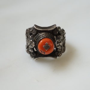 May include: A silver ring with an orange stone set in the center. The ring is decorated with intricate floral designs.