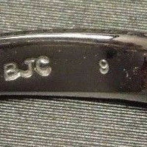 May include: Close-up of a black band with the inscription "14K BJC 9" on the inside.