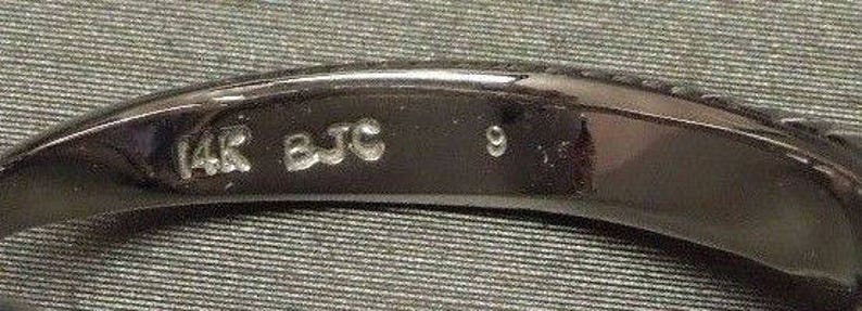 May include: Close-up of a black band with the inscription "14K BJC 9" on the inside.