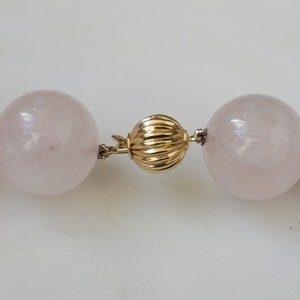May include: A pink rose quartz necklace with a gold clasp. The necklace is made of large, round beads.