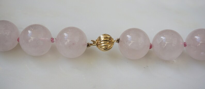 May include: A pink rose quartz necklace with a gold clasp. The necklace is made of large, round beads.