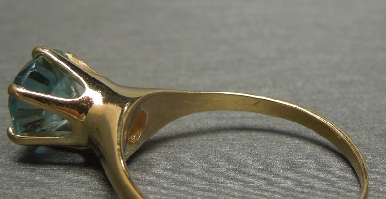 May include: A gold ring with a large, light blue gemstone set in a prong setting.