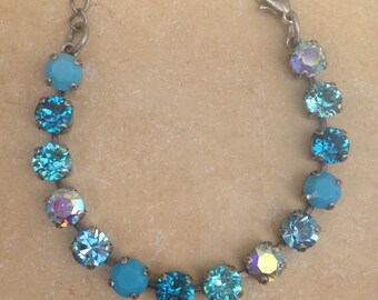 May include: A bracelet with a series of round, light blue and iridescent crystals. The crystals are linked by a thin, silver-toned chain and clasp. The bracelet is designed to be worn around the wrist.