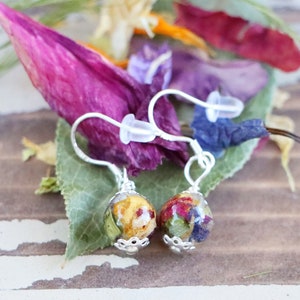May include: A pair of silver earrings with small round glass beads filled with pressed flowers. The beads are filled with a variety of colors, including yellow, red, and blue.