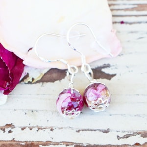 May include: A pair of silver earrings with pink and white flower petals encased in clear resin. The earrings have a simple hook closure.