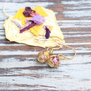 May include: A pair of gold earrings with small round glass beads filled with pressed flowers in shades of pink, purple, and yellow.