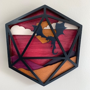 Op de afbeelding: Een houten, zwart geframed, geometrisch, veelkleurig, 3D wandkunstwerk dat een draak voorstelt die in een zonsonderganglucht vliegt.