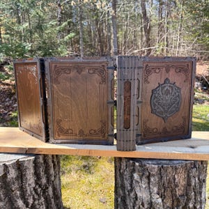 May include: A folding wooden screen with four panels featuring dark brown wood grain, intricate Celtic-style corner engravings, and a central spine with the text "Tales Shall Woven". The right panel displays a prominent circular dragon emblem.