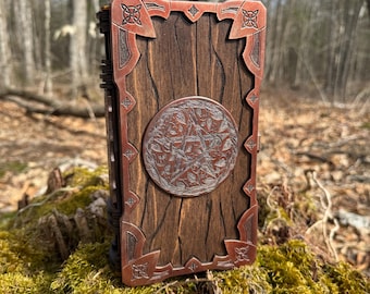 May include: A rectangular wooden box featuring a dark brown wood grain finish. The box is adorned with metallic copper-colored corner accents and a central circular medallion, both displaying intricate engraved knotwork and pentagram designs.