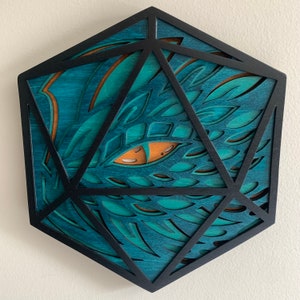 Op de afbeelding: Een houten, zwart geframed, teal-kleurig, drakenoogvormig, geometrisch wandkunstwerk.