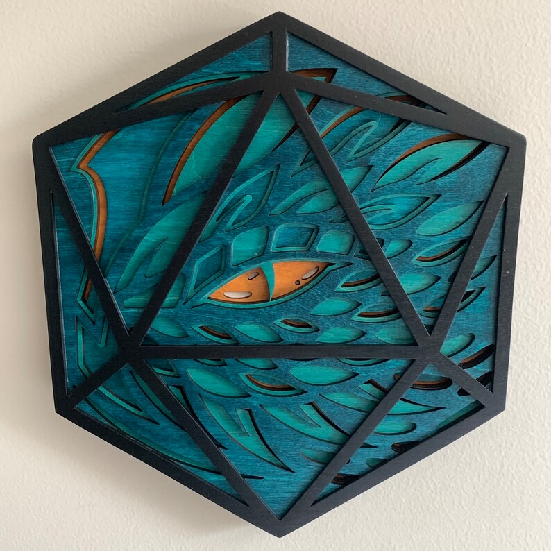 Op de afbeelding: Een houten, zwart geframed, teal-kleurig, drakenoogvormig, geometrisch wandkunstwerk.