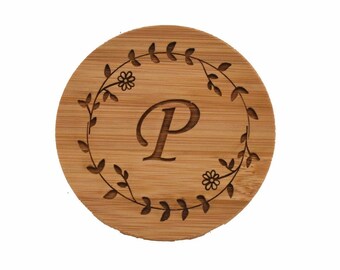 May include: A round wooden coaster with a floral wreath design and the letter "P" in the center.
