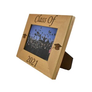 Op de afbeelding: Een houten fotolijst met een afstudeerhoedontwerp en de tekst "Class of 2021".