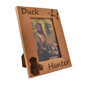 Puede incluir: Un marco de fotos de madera con una foto de un perro que recupera patos. El marco est&aacute; grabado con las palabras "Duck Hunter" y una silueta de un pato.