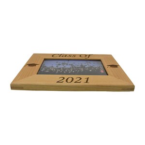 Op de afbeelding: Een houten fotolijst met de tekst "Class of 2021" gegraveerd op de voorkant. De lijst heeft een afstudeerhoedje gegraveerd in elke hoek.