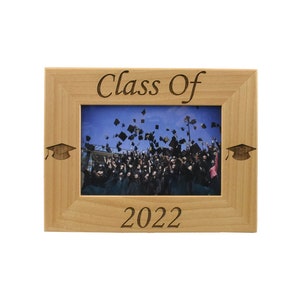 Op de afbeelding: Een houten fotolijst met de tekst "Class of 2022" en afstudeerhoeden aan beide kanten. De lijst bevat een foto van een afstudeerceremonie met studenten die hun hoeden in de lucht gooien.