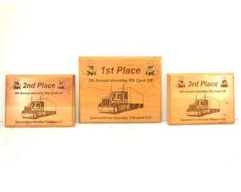 May include: Three wooden plaques with engraved text and images. The plaques are for 1st, 2nd, and 3rd place in a rib cook-off. Each plaque features a cartoon chef and a semi-truck. The text reads "5th Annual elmvalley Rib Cook Off" and "Sponsored by elmvalley Transport LLC".