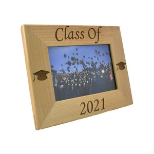 Op de afbeelding: Een houten fotolijst met de tekst "Class of 2021" gegraveerd aan de onderkant. De lijst heeft twee afstudeerhoeden in de bovenste hoeken gegraveerd.