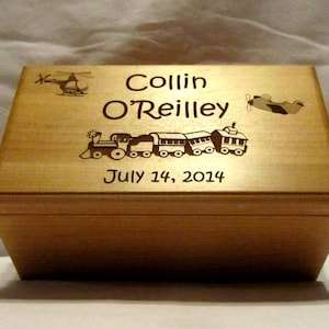 Puede incluir: Una caja de madera para recuerdos con un diseño grabado que presenta un tren, un avión y un helicóptero. La caja está personalizada con el nombre "Collin O'Reilly" y la fecha "14 de julio de 2014".