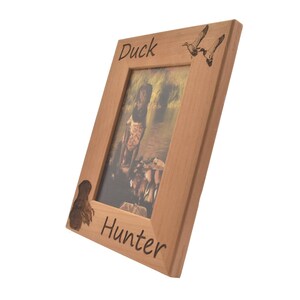 Puede incluir: Un marco de fotos de madera con un perro marr&oacute;n y patos grabados en &eacute;l. El marco dice "Duck Hunter" en la parte inferior.