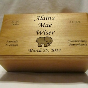 Puede incluir: Una caja de madera para recuerdos con un diseño de elefante grabado y el texto "Alaina Mae Wiser", "March 25, 2014", "21-1/2 Inches", "9 pounds 15 ounces", "4:31 p.m." y "Chambersburg, Pennsylvania".