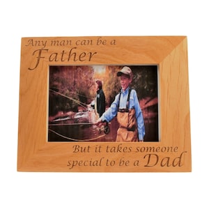 May include: A wooden picture frame with an engraved message that reads "Any man can be a Father, But it takes someone special to be a Dad". The frame has a photo of two people fishing in a stream.