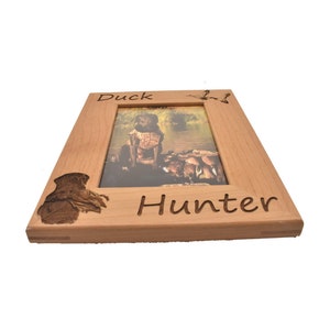Puede incluir: Un marco de fotos de madera con un pato tallado y las palabras "Duck Hunter". El marco es de color marr&oacute;n claro y tiene un acabado de madera natural.