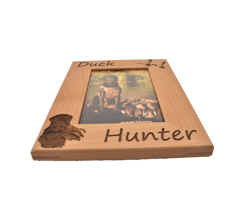 Puede incluir: Un marco de fotos de madera con un pato tallado y las palabras "Duck Hunter". El marco es de color marr&oacute;n claro y tiene un acabado de madera natural.