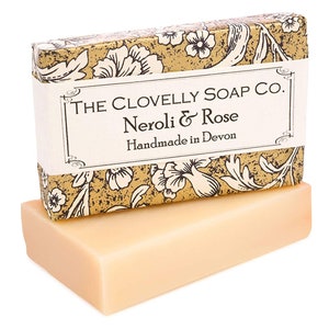 May include: A bar of soap in a box. The box is gold with a floral pattern and the text "THE CLOVELLY SOAP CO. Nerolli & Rose Handmade in Devon".