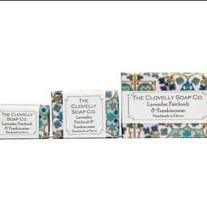 May include: Three bars of soap with a blue and gold patterned design. The soap is labelled "The Clovelly Soap Co." and "Lavender, Patchouli & Frankincense". The soap is handmade in Devon.