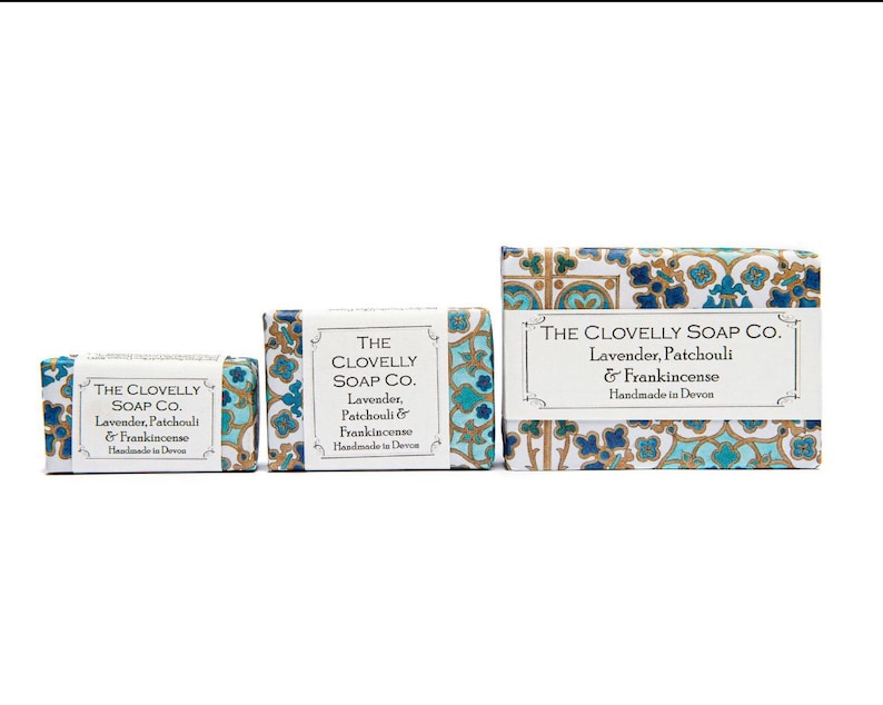 May include: Three bars of soap with a blue and gold patterned design. The soap is labelled "The Clovelly Soap Co." and "Lavender, Patchouli & Frankincense". The soap is handmade in Devon.