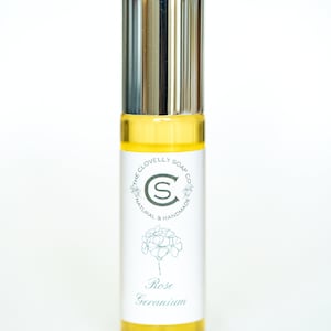May include: A glass bottle of essential oil with a silver cap and a white label. The label has a floral design and the text "The Clovelly Soap Co. Natural & Handmade Rose Geranium".