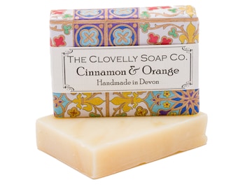 Puede incluir: Una pastilla de jabón en una caja blanca con un diseño estampado de colores. La caja tiene una etiqueta que dice "The Clovelly Soap Co. Cinnamon & Orange Handmade in Devon."