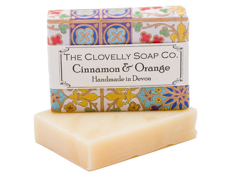 May include: A bar of soap in a white box with a colourful patterned design. The box has a label that reads "The Clovelly Soap Co. Cinnamon & Orange Handmade in Devon."