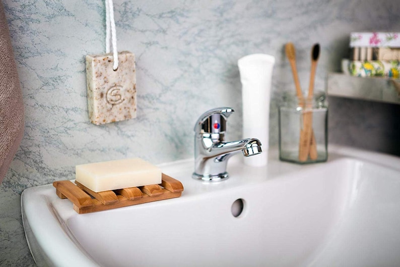 May include: A white porcelain bathroom sink with a chrome faucet. A bar of soap is on a wooden soap dish. Two wooden toothbrushes are in a glass jar on the counter.