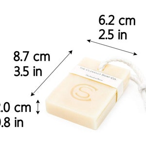 Puede incluir: Una barra de jab&oacute;n rectangular con una cuerda blanca atada. El jab&oacute;n est&aacute; etiquetado con "The Clovelly Soap Co. Handmade in Devon". El jab&oacute;n mide 8,7 cm de largo, 6,2 cm de ancho y 2 cm de grosor.