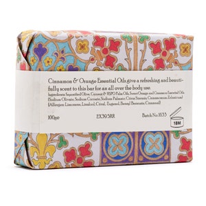 May include: A bar of soap wrapped in colourful patterned paper. The label reads "Cinnamon & Orange Essential Oils give a refreshing and beautifully scent to this bar for an all over the body use." The ingredients are listed, including saponified olive, coconut, and RSPO palm oils, sweet orange and cinnamon essential oils. The label also includes the batch number 1633 and a 18M symbol.