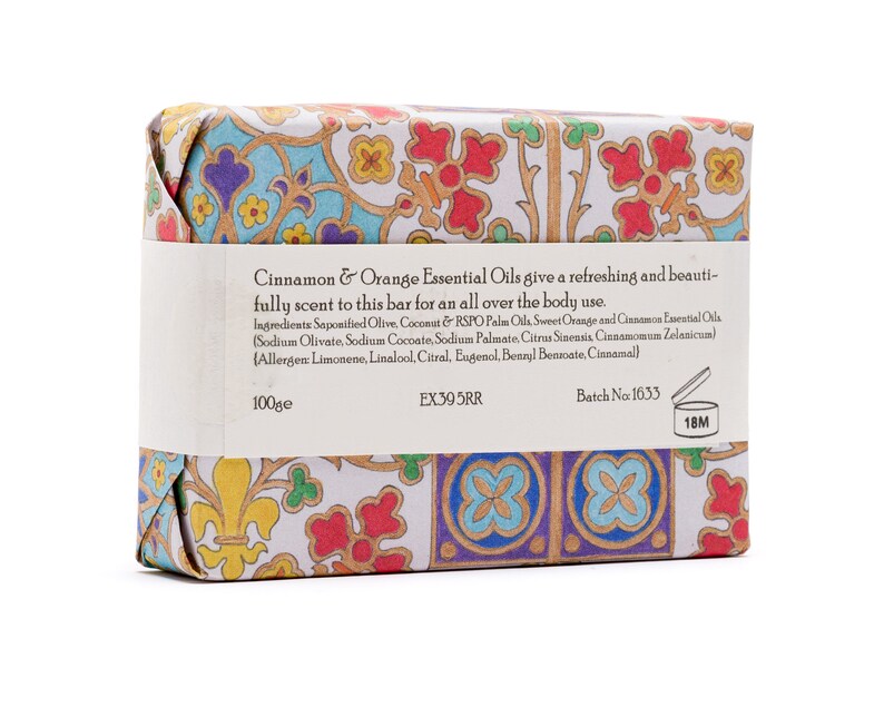 May include: A bar of soap wrapped in colourful patterned paper. The label reads "Cinnamon & Orange Essential Oils give a refreshing and beautifully scent to this bar for an all over the body use." The ingredients are listed, including saponified olive, coconut, and RSPO palm oils, sweet orange and cinnamon essential oils. The label also includes the batch number 1633 and a 18M symbol.