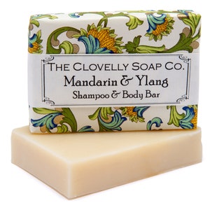 Peut inclure: Une barre de savon blanche avec un emballage à motifs floraux. L'emballage porte le texte "THE CLOVELLY SOAP CO. Mandarin & Ylang Shampoo & Body Bar".