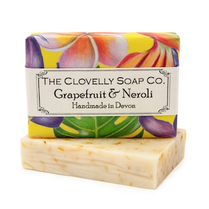 May include: A bar of soap wrapped in yellow paper with a floral design and a label that reads "THE CLOVELLY SOAP CO. Grapefruit & Neroli Handmade in Devon".