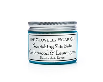 May include: A blue jar with a silver lid containing a nourishing skin balm. The label reads "The Clovelly Soap Co. Nourishing Skin Balm Cedarwood & Lemongrass Handmade in Devon."
