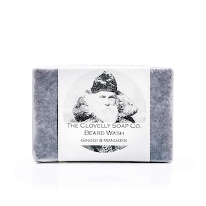 May include: A bar of soap with a black and white image of a man with a beard and a hat. The soap is labeled "The Clovelly Soap Co. Beard Wash Ginger & Mandarin."