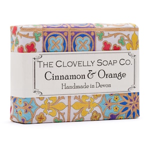 May include: A bar of soap with a colourful, patterned wrapper. The wrapper features a label that reads "THE CLOVELLY SOAP CO. Cinnamon & Orange Handmade in Devon."
