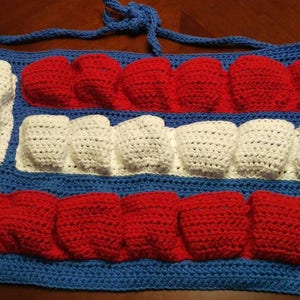 May include: A crocheted egg holder with red, white, and blue stripes. The holder has a strap for carrying.