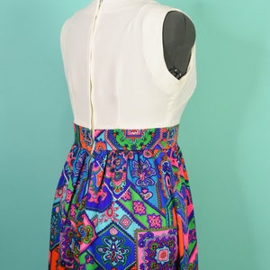 May include: A white sleeveless dress with a colorful geometric print skirt. The skirt features a variety of colors, including blue, green, pink, and orange.