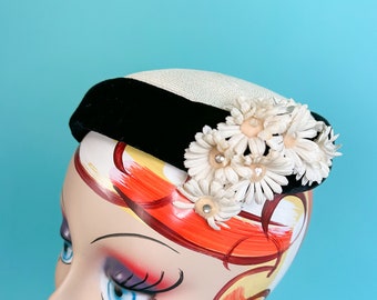 May include: A black velvet and white straw hat with a cluster of white fabric flowers.